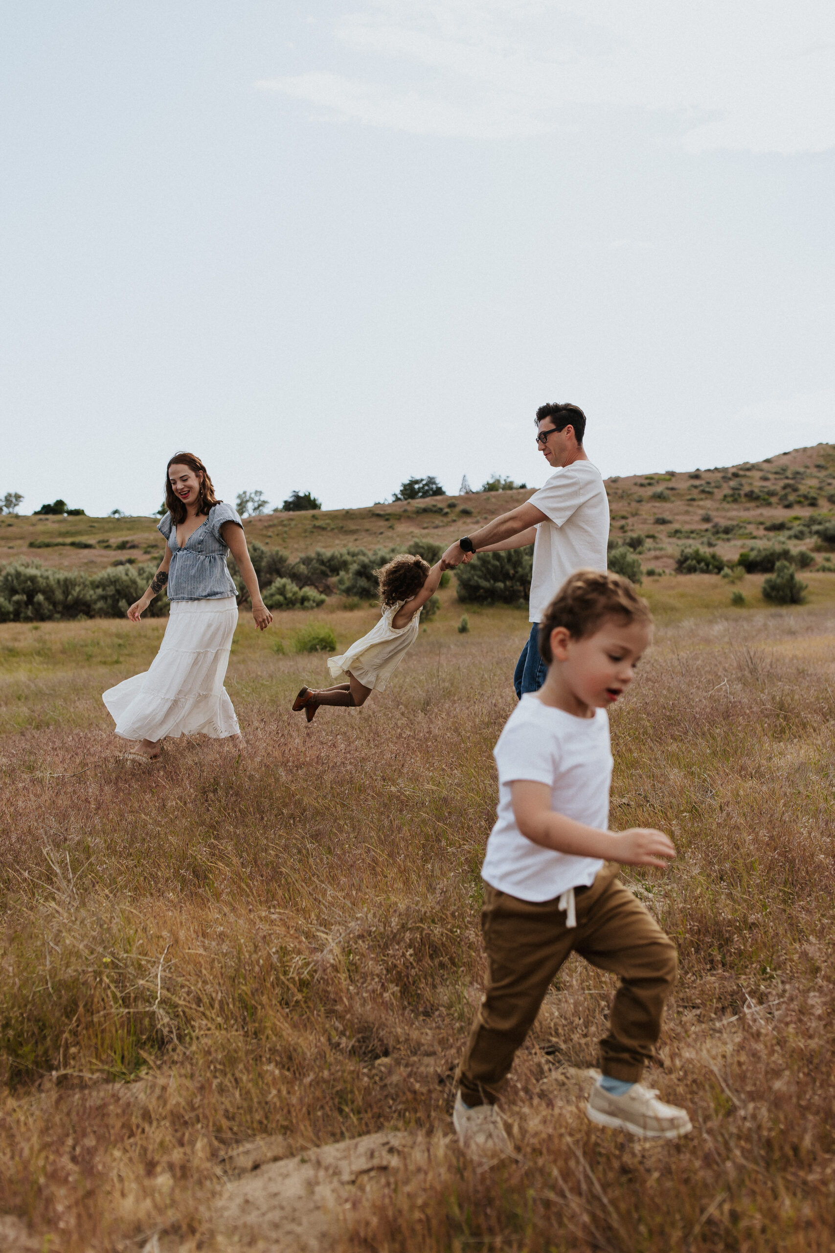 Boise family session in the Idaho countryside with parents walking hand in hand with their children through tall grass.